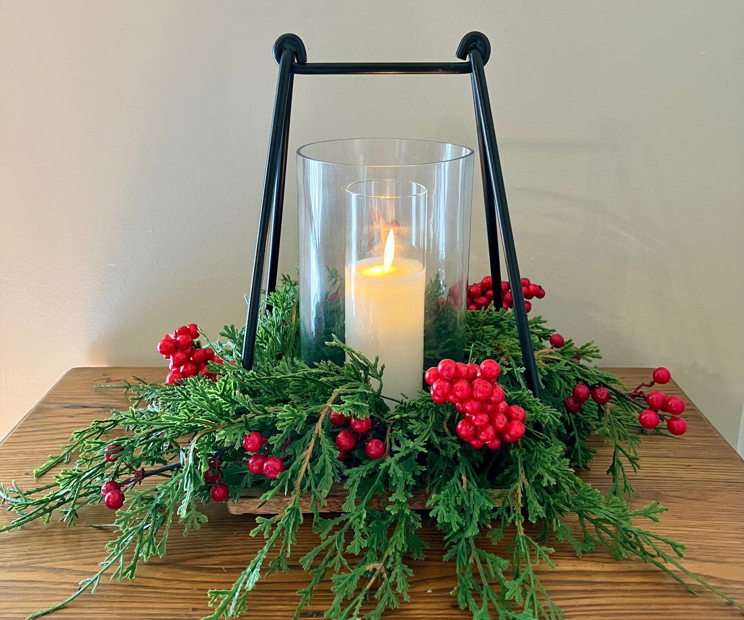 Decorative candle holder with greenery and red berries on a wooden surface.