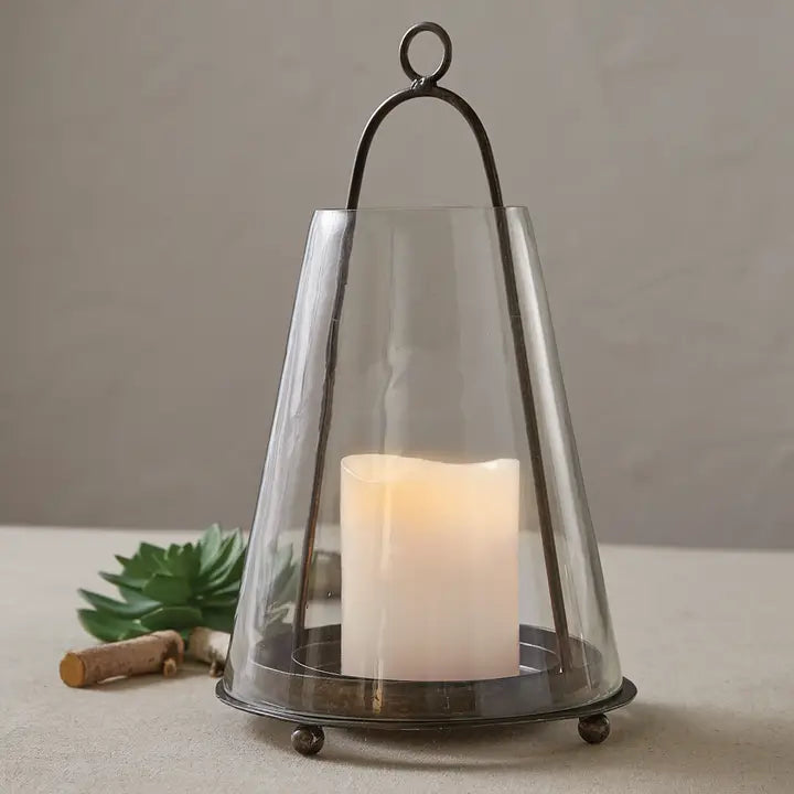 Hanging tapered lantern is made of a metal base with tapered glass enclosure