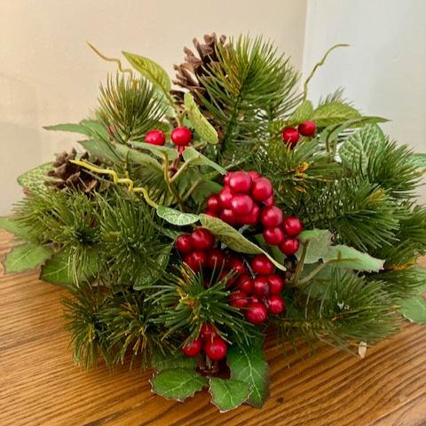 A half sphere with a mix of pine and holly leaves, red berries and pinecones.