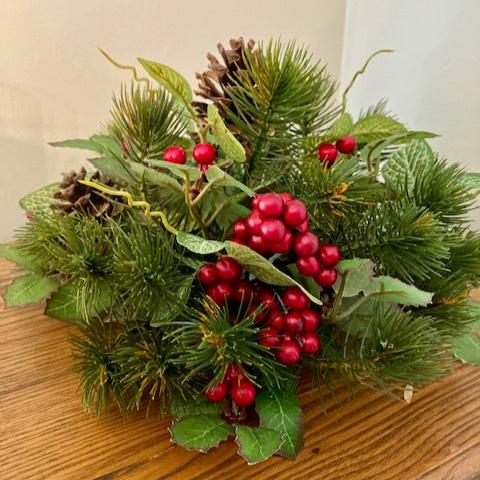 A half sphere with a mix of pine and holly leaves, red berries and pinecones. 