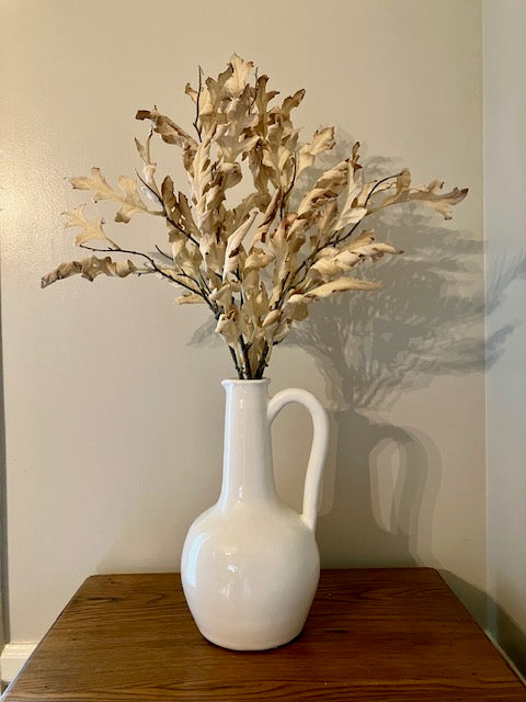 Long neck ceramic pitcher in white. Shown with cream dried leaf stems. 